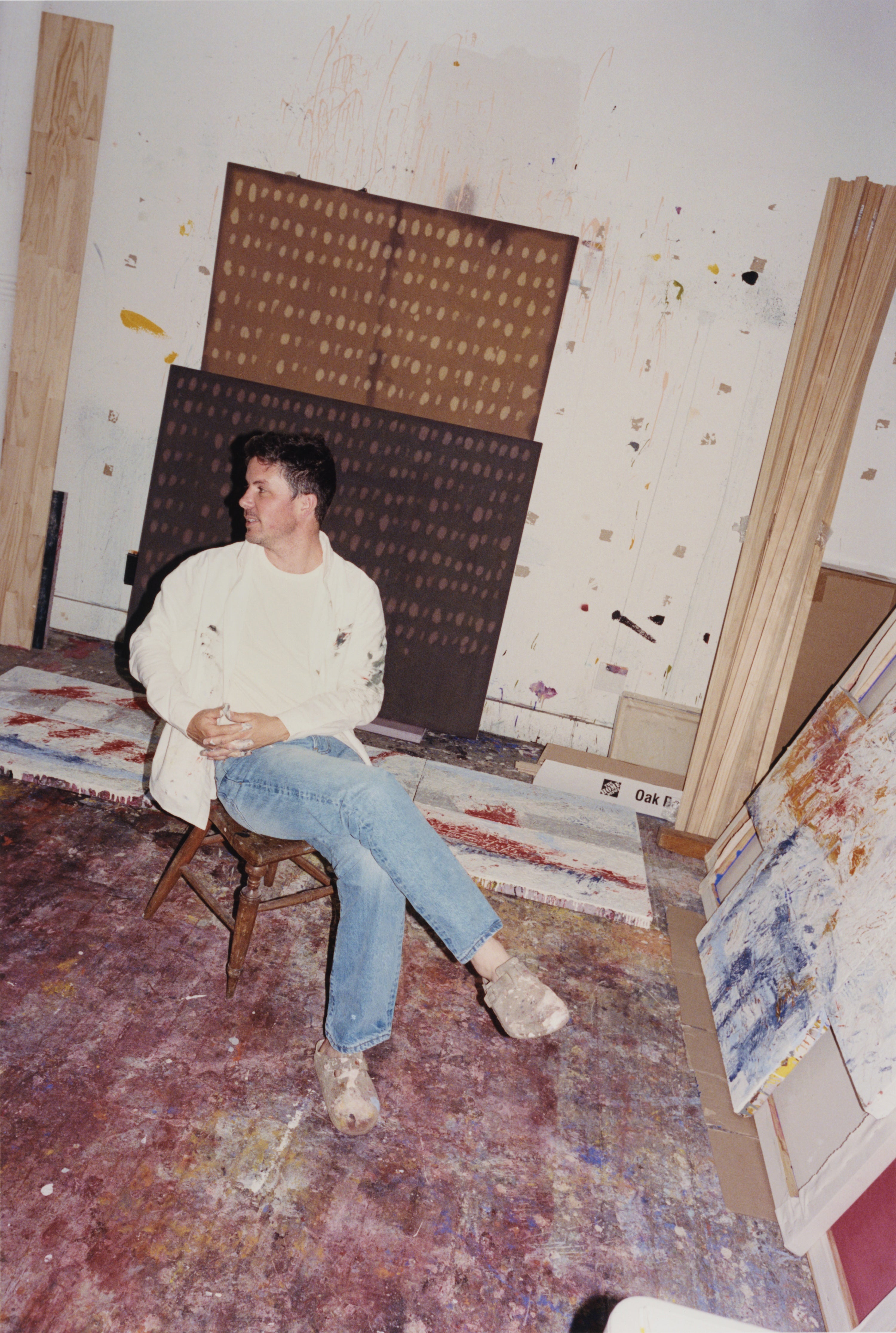 Artist Joe Henry Baker sitting in his studio in front of his paintings