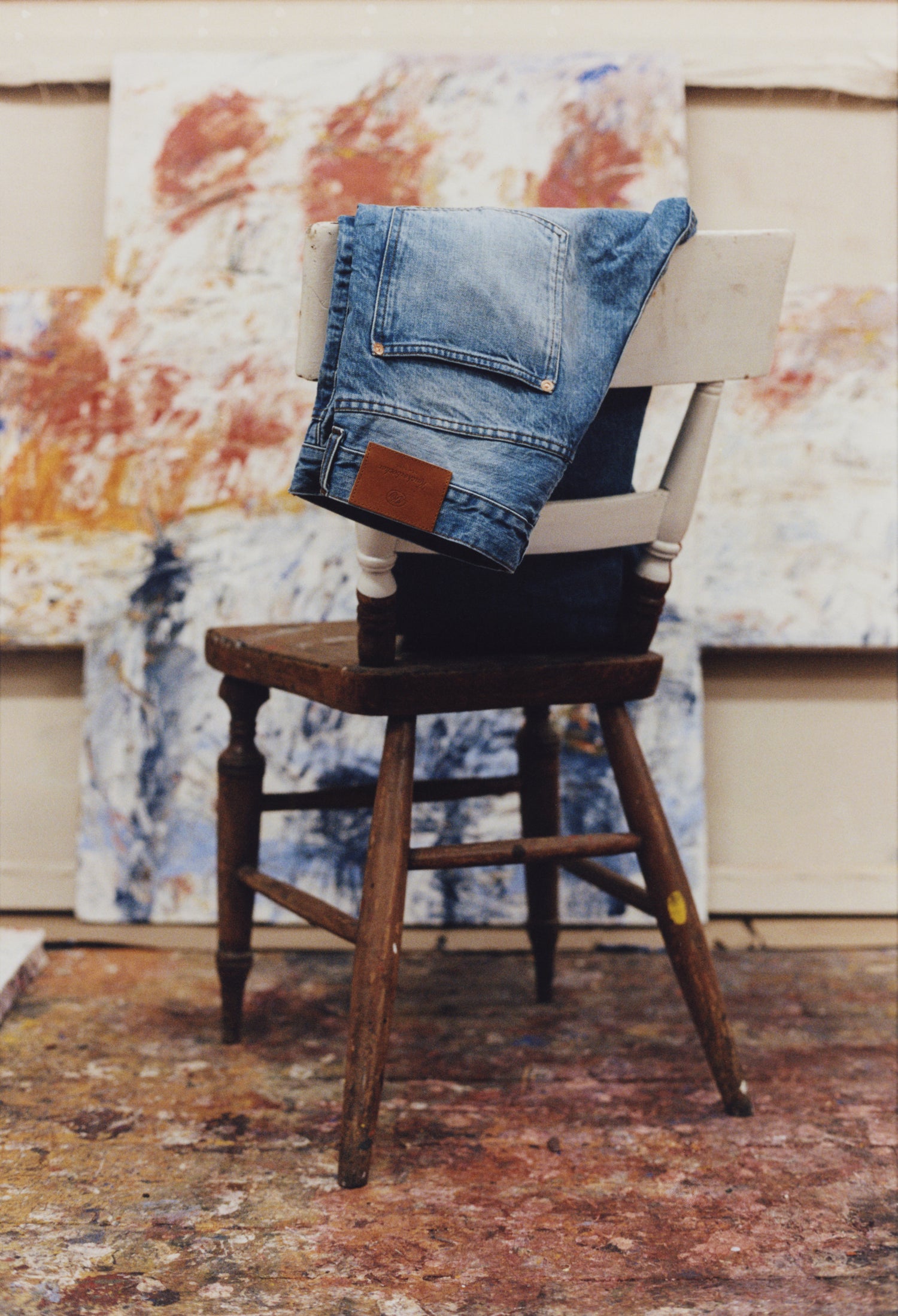Blue denim jacket on a wooden chair with a colorful abstract painting in the background
