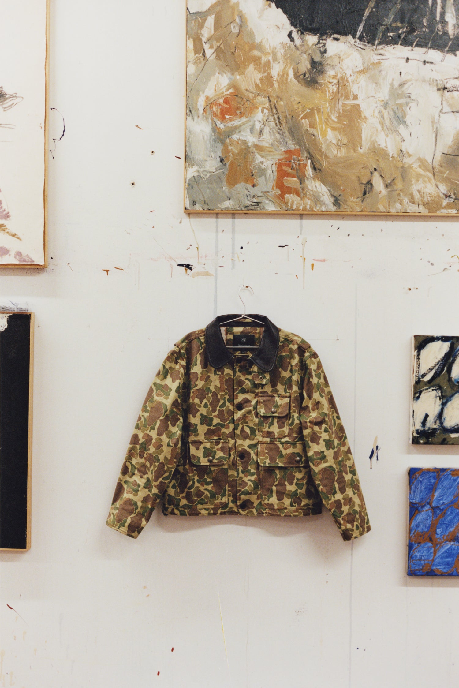 Camouflage jacket hanging on a white wall with abstract art in the background