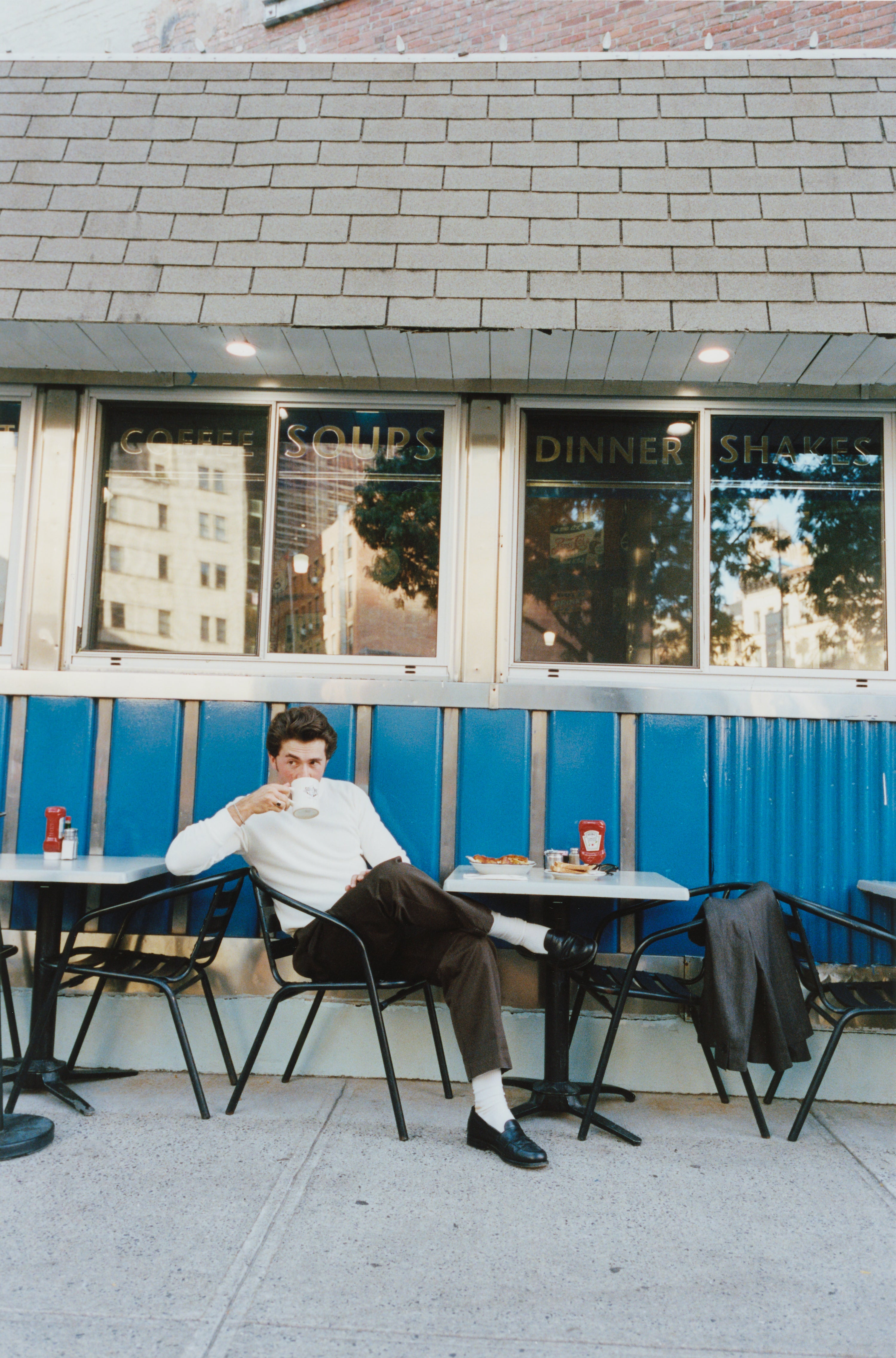 Albert Muzquiz drinking coffee outside a diner and wearing a thermal.