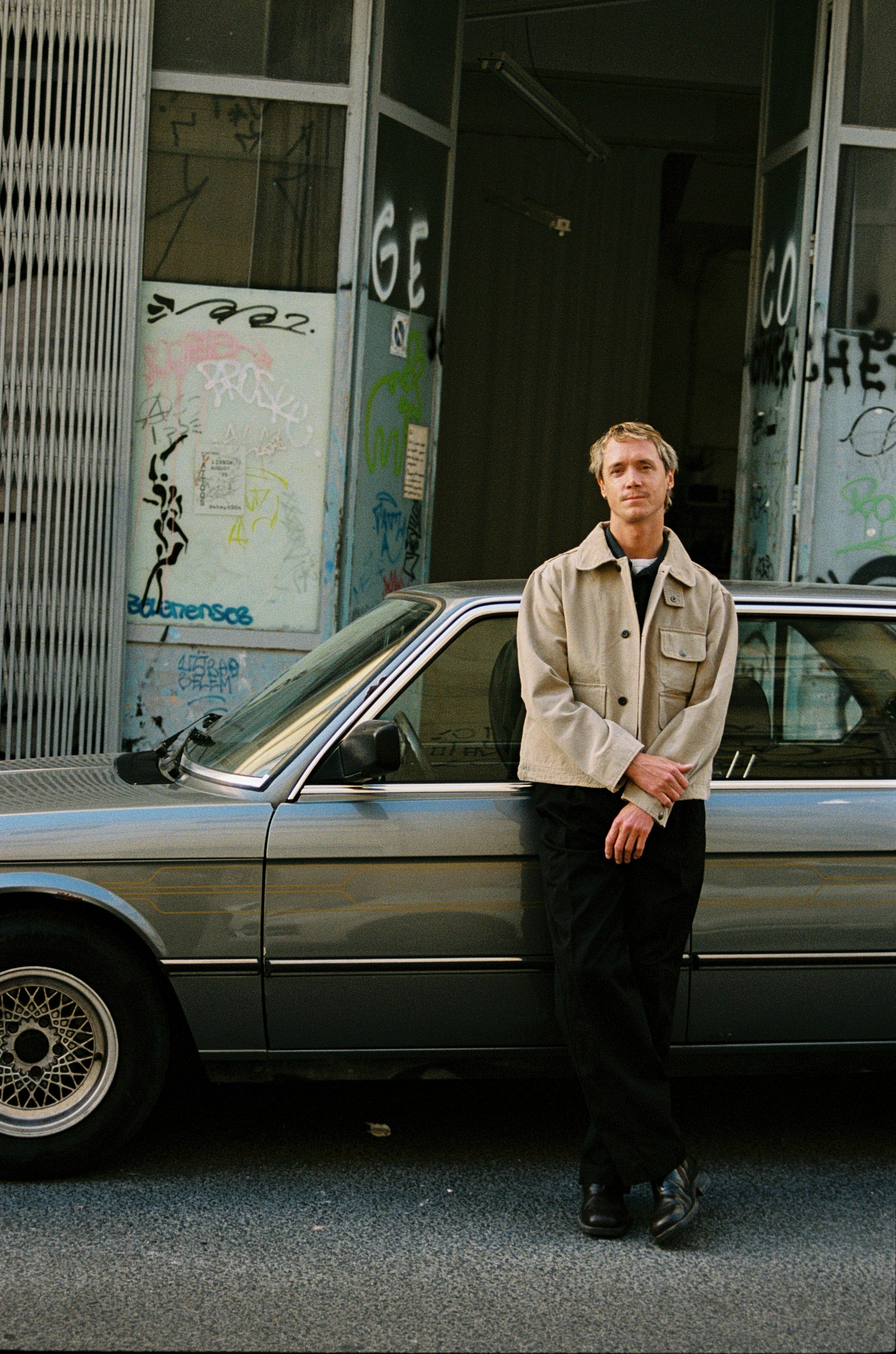Guy in khaki jacket standing by car.