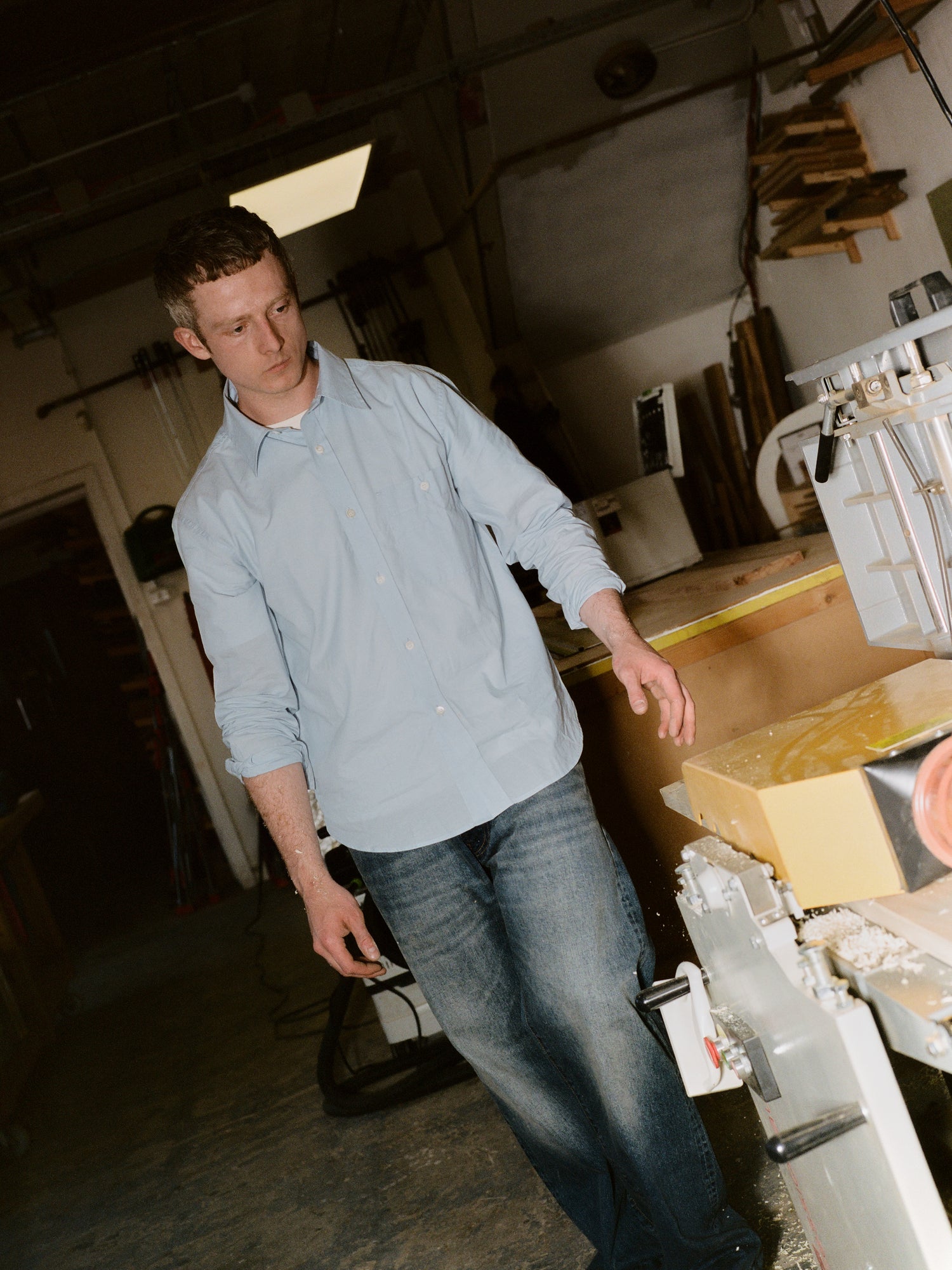 Man in a light blue shirt and jeans standing in a workshop or storage area.