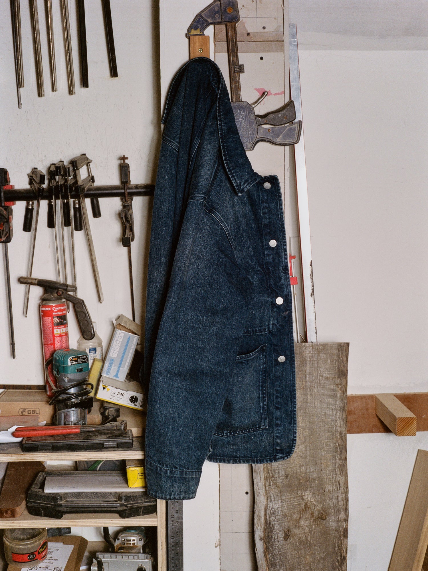 Blue denim jacket hanging on a wooden post in a workshop with tools and equipment.