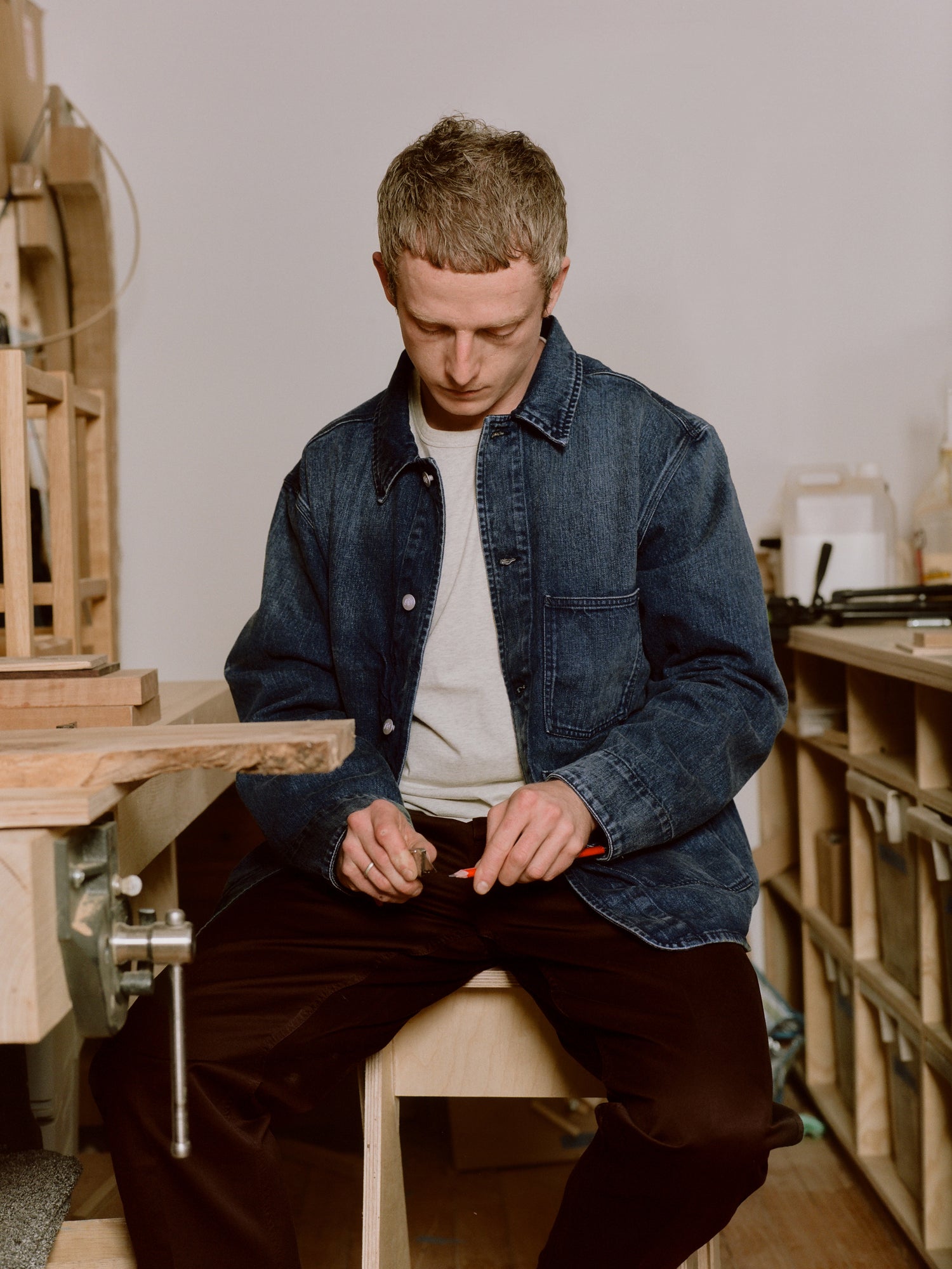 Man sitting on a stool in a workshop wearing a denim jacket.